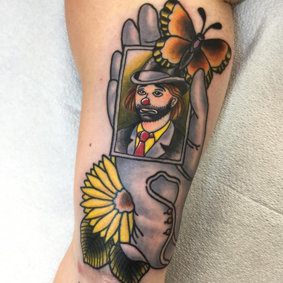 A tattooed image of a clown's portrait in a gloved hand beside a flower and butterfly